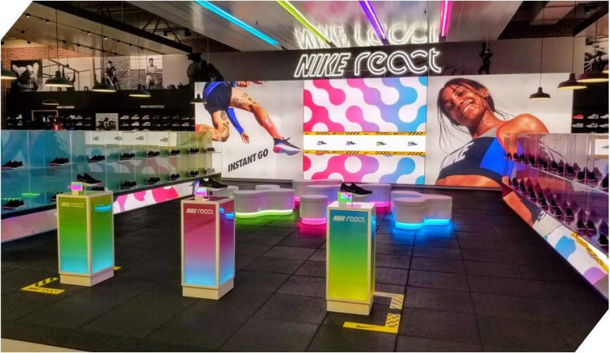 Colorful Nike React in-store display showcasing vibrant lighting, athletic visuals, and featured footwear on illuminated pedestals.