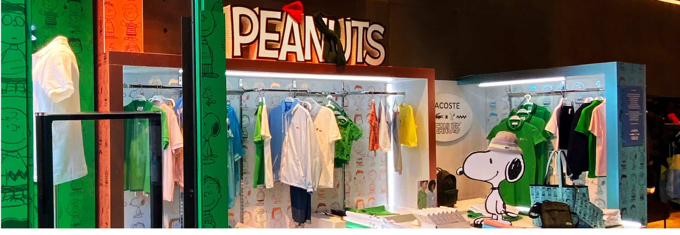Lacoste x Peanuts clothing display featuring colorful garments, themed illustrations, and Snoopy visuals.