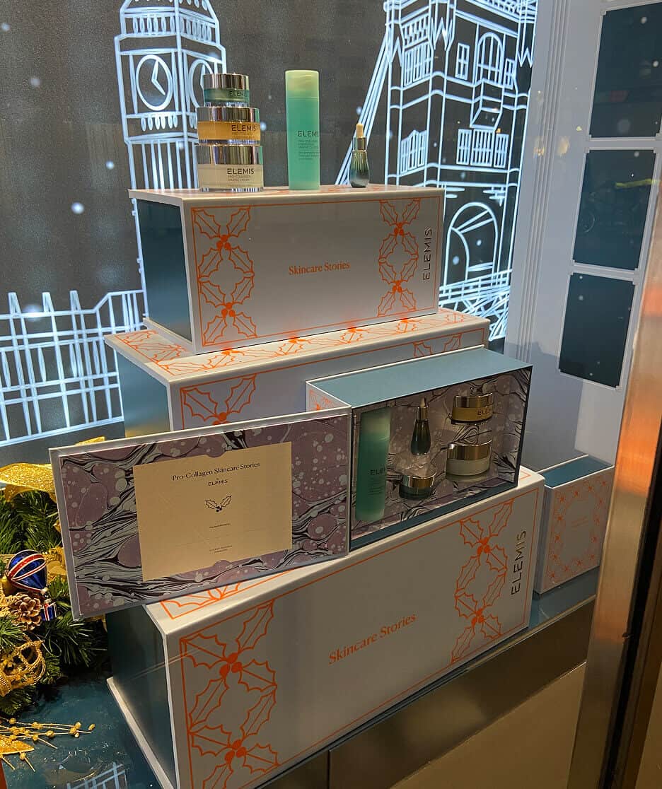 Stacked Elemis “Skincare Stories” gift boxes on festive display with London-themed illustrations in the background.