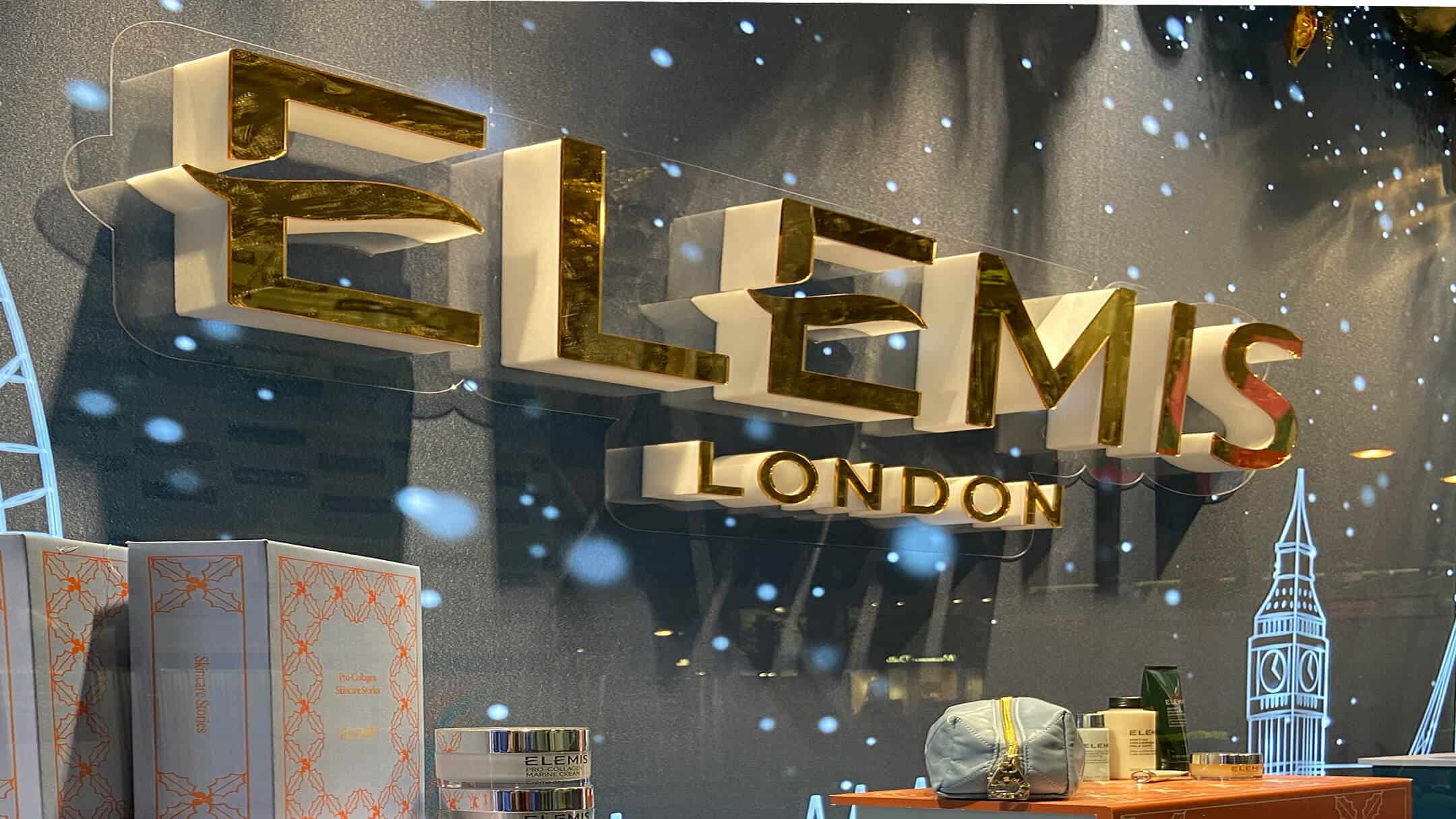 Close-up of an Elemis London retail window display with golden 3D signage and skincare gift sets.