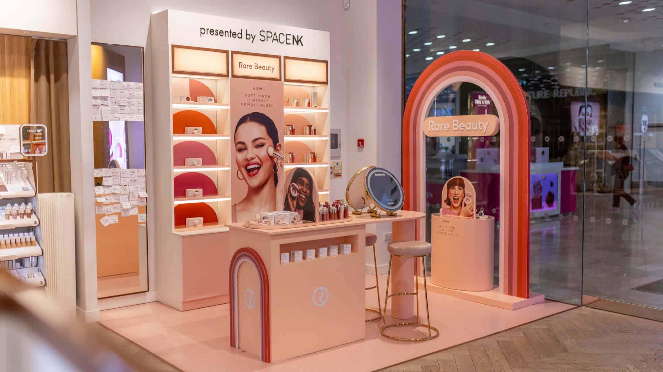 Curved rainbow-themed arch featuring the Rare Beauty logo by Selena Gomez at a retail pop-up entrance.