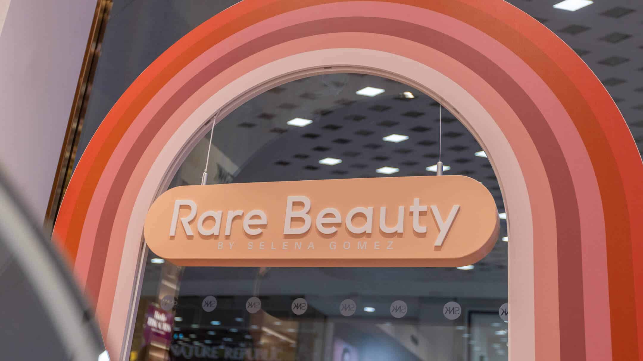 Curved rainbow-themed arch featuring the Rare Beauty logo by Selena Gomez at a retail pop-up entrance.